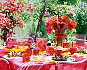 Summery table set with poppies in glass vases and a water bowl and hurricane candles with flower petals