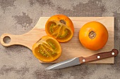 Fresh naranjillas on a chopping board with a knife