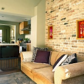 Suite of rooms in a country home: living room with sofa against a brick wall, kitchen with island and dining nook