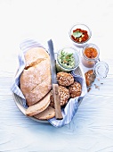 White bread and seeded bread rolls in a bread basket, with various spreads