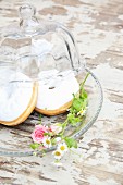 Donuts decorated with white icing and flowers on glass plate with glass cover