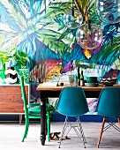 Dining table, various chairs and spherical glass lamps in front of jungle patterned wallpaper