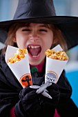 A girl holding paper cones of caramelised popcorn for Halloween