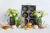 Mini cakes and confectionery in front of an old baking tin and vases of flowers