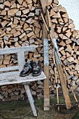 Vintage Skiausrüstung auf verwitterter Holzbank vor Brennholzstapel an Hauswand