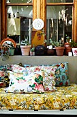 Floral cushions and mattress on couch in front of potted plants on window sill