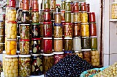 Lots of jars of assorted preserved food and mounds of olives in a shop