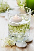 Floating candle and elderberry flowers in glass