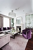 Elegantes Wohnzimmer mit samtbezogenen Polstermöbeln in Grau und Violett; in der Mitte ein quadratischer Couchtisch mit spiegelnder Oberfläche