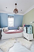 Cheerful child's bedroom with large dolls' house and soft animal-skin rugs on floor next to bed