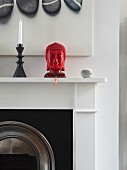 Roter Buddhakopf aus Porzellan neben schwarzem Kerzenhalter auf Kaminsims