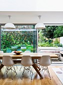 Classic chairs and modern wooden dining table in front of open terrace door with view of terrace and garden