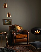 Winter shopping trends: leather armchair with scatter cushions, side table, Persian rug, floor cushion, stove, picture and pendant lamps