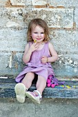 Little girl sitting on wooden bench against wall