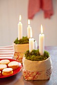 Kerzen im Leinensack mit Moos, daneben Plätzchenteller