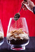 A woman drizzling honey onto a layered dessert of chocolate cake, cream and oat biscuits