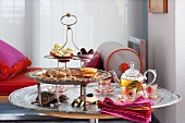 Tiered cake stand with assorted baked goods, a teapot and elegant glass teacups