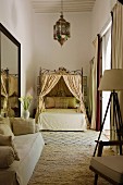 Moroccan bedroom in shades of cream with sofa, canopied bed and lantern-shaped ceiling lamp