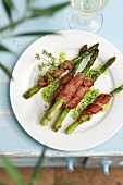 Grilled green asparagus wrapped in bacon with a herb sauce