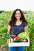 Portrait of young woman holding box of fresh vegetables in allotment