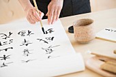 Woman painting Oriental characters on roll of paper using paintbrush