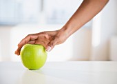 A hand reaching for a green apple