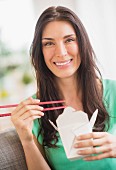 A woman eating Asian food out of a takeaway carton, using chopsticks