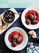 Mondeghili (meatballs from Milan) in tomato sauce with a dish of black olives