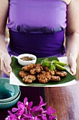 A woman carrying a plate of Thai fishcakes