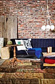 Rustikaler Holz Beistelltisch auf Patchwork Teppich vor dunkelblauem Sofa an rustikaler Ziegelwand; Hängeleuchte mit gebündelten, kugelförmigen Schirmen