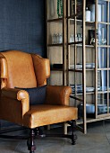 Light brown leather armchair next to display cabinet with open door against dark blue wall