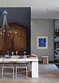 Set, modern dining table below designer pendant lamp in front of antique cupboard against grey wall