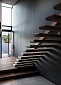 Floating stair treads protruding from wall in minimalist stairwell with open terrace door