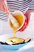 A woman pouring mustard marinade onto sliced aubergine