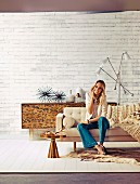 Blonde woman sitting on sofa in front of retro, leopard-patterned sideboard