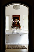 View through doorway of free-standing bathtub, flowers on shelf & picture on wall