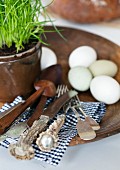 Hand-carved salad servers and old silver cutlery with flat handles and horn handles on black and white gingham napkin; eggs and potted chives on stoneware plate