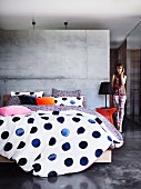 Bed linen with blue polka dots on double bed against concrete partition wall in minimalist sleeping area
