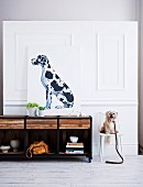 Hundeportrait auf Sideboard und kleiner weisser Hund auf Stuhl vor weisser Holzpaneelwand