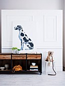 Portrait of dog on top of sideboard and small, white dog sitting on chair against white, wood-panelled wall