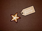 Star shaped ginger bread biscuit with white icing, and Christmas gift-tag, on a brown background