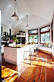 Light-flooded kitchen with wooden floor & retro pendant lamps hanging from white wooden ceiling above island counter