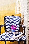 Postmodern chair with white and blue upholstery and black wooden frame against yellow wall draped in lace fabric