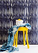 Hand-dyed cloth and yellow-painted stool against blue and white striped wall