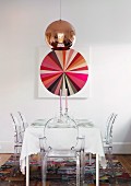 Copper pendant lamp above festively set table with Ghost chairs and picture of colour wheel on wall
