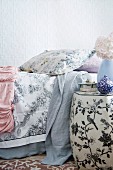 Detail of a boudoir - Side table painted with flowers and birds next to bed with bedspreads and throws