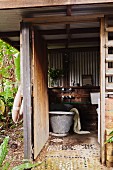 Outdoor bathroom with zinc bathtub in wooden structure with corrugated metal cladding and pebble mosaic floor