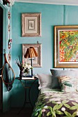 Second-hand lamp on old, iron bedside table next to bed and gallery of pictures on turquoise-painted wall