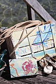 Old fruit crates painted with summery, maritime motifs in acrylic paint on wooden jetty on lake shore