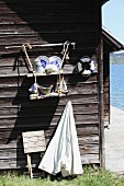 Blue and white crockery on DIY suspended shelves made from wooden boards and jute rope on outside wall of boathouse